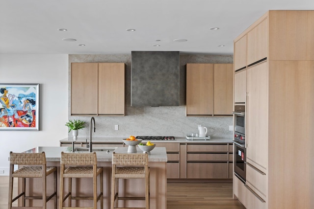 kitchen with a breakfast bar area, light brown cabinets, a sink, wood finished floors, and decorative backsplash