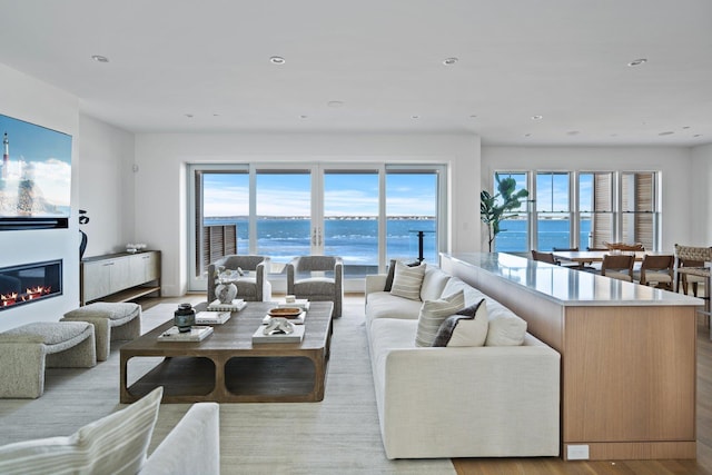 living room featuring a water view, recessed lighting, wood finished floors, and a glass covered fireplace