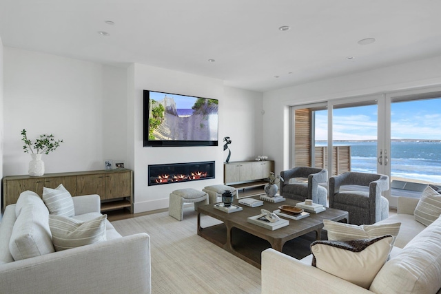 living area with baseboards, light wood-type flooring, a glass covered fireplace, and recessed lighting