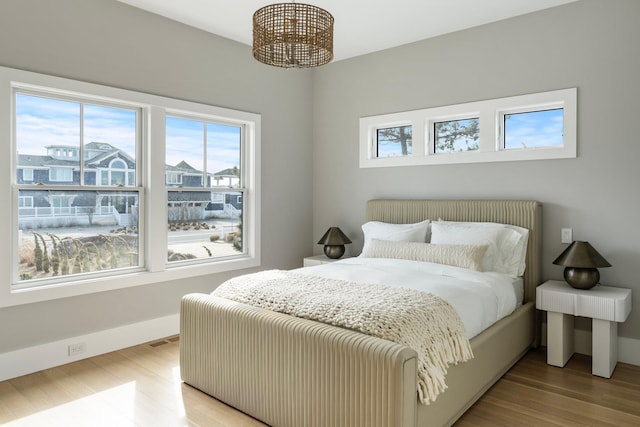 bedroom with baseboards, light wood finished floors, visible vents, and an inviting chandelier