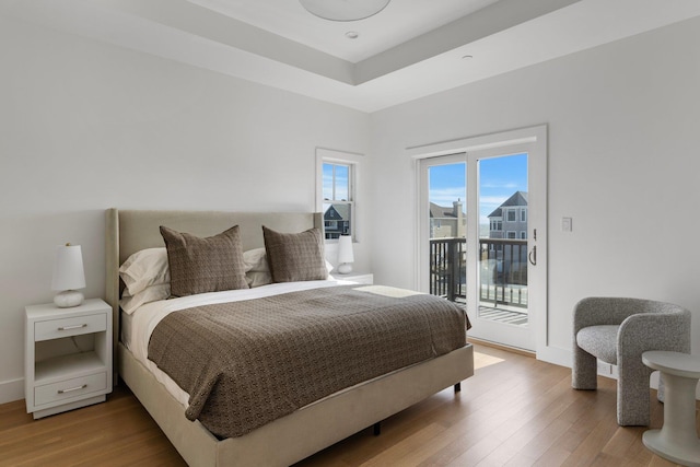 bedroom with access to exterior, a tray ceiling, and wood finished floors