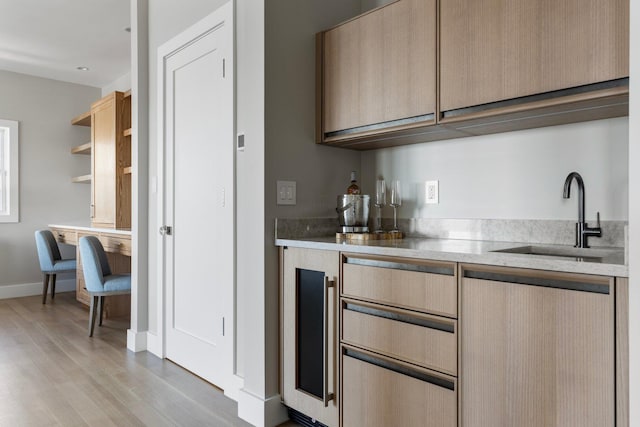 bar featuring light wood-style floors, bar, baseboards, and a sink