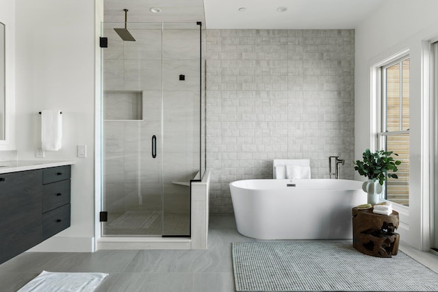 full bathroom featuring tile patterned flooring, vanity, tile walls, a freestanding bath, and a stall shower