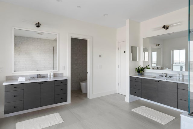 bathroom with two vanities, a sink, toilet, and baseboards