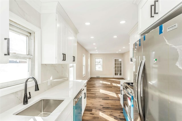 kitchen with decorative backsplash, stainless steel appliances, wood finished floors, white cabinetry, and a sink