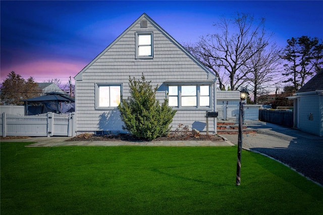 property exterior at dusk featuring fence, a lawn, and a gate