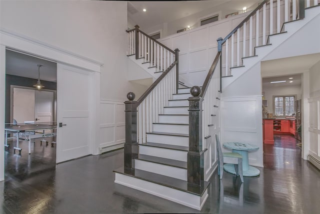 stairs with a decorative wall, a wainscoted wall, a towering ceiling, and a baseboard radiator