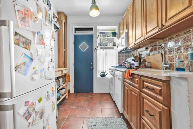 kitchen with decorative backsplash, brown cabinetry, a sink, white appliances, and tile patterned floors