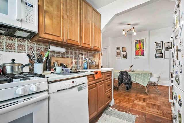 kitchen featuring white appliances, brown cabinetry, backsplash, light countertops, and a sink