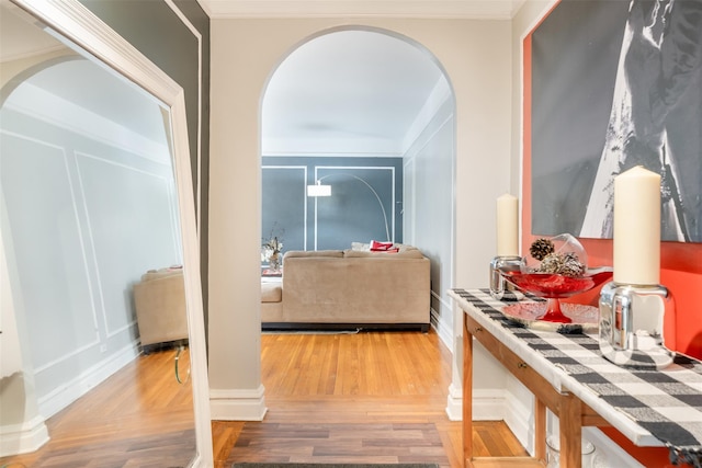 hall featuring arched walkways, ornamental molding, a decorative wall, and wood finished floors