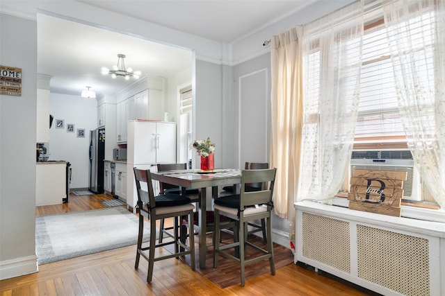 dining area featuring a notable chandelier, baseboards, light wood-style flooring, and radiator