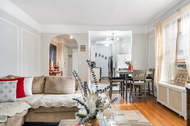 living room featuring radiator, light wood finished floors, arched walkways, and a notable chandelier