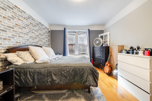 bedroom featuring brick wall, wood finished floors, and an accent wall