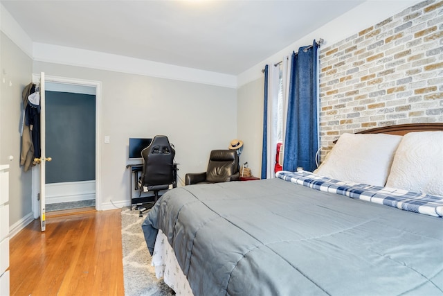 bedroom with brick wall, baseboards, and wood finished floors