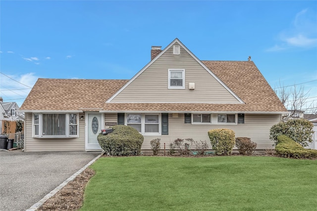 view of front facade featuring a shingled roof, a chimney, a front lawn, and aphalt driveway