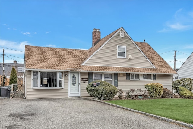 view of front of house featuring aphalt driveway, a shingled roof, fence, a front lawn, and a chimney