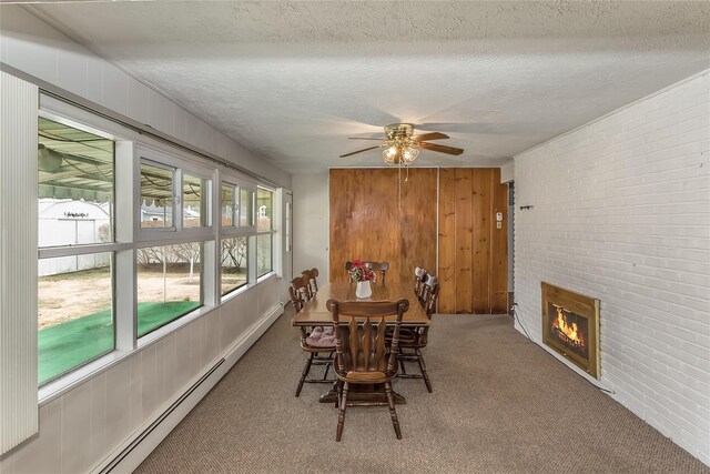 carpeted dining room with a ceiling fan, brick wall, baseboard heating, a textured ceiling, and a brick fireplace