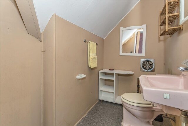 half bath with toilet, baseboards, vaulted ceiling, and a sink