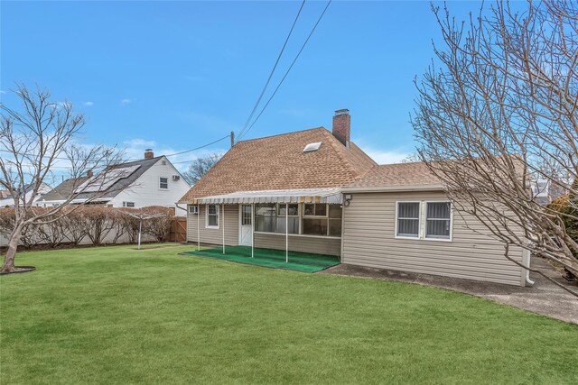 back of property with a shingled roof, a chimney, fence, and a yard