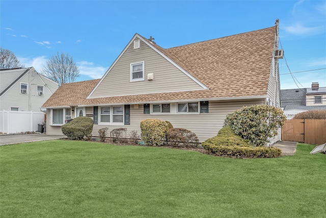 view of front facade featuring a shingled roof, a front yard, and fence