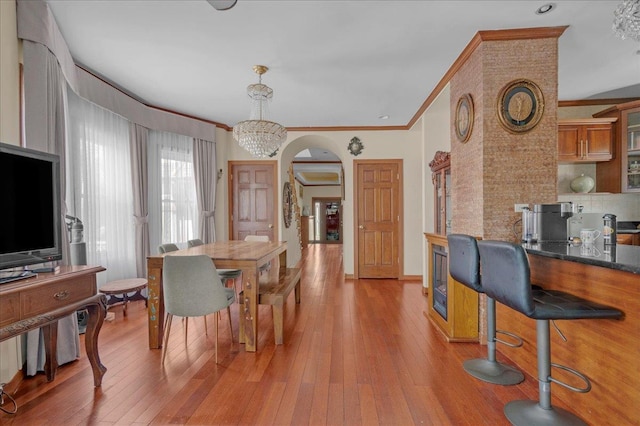 dining space with crown molding, light wood-type flooring, arched walkways, and an inviting chandelier