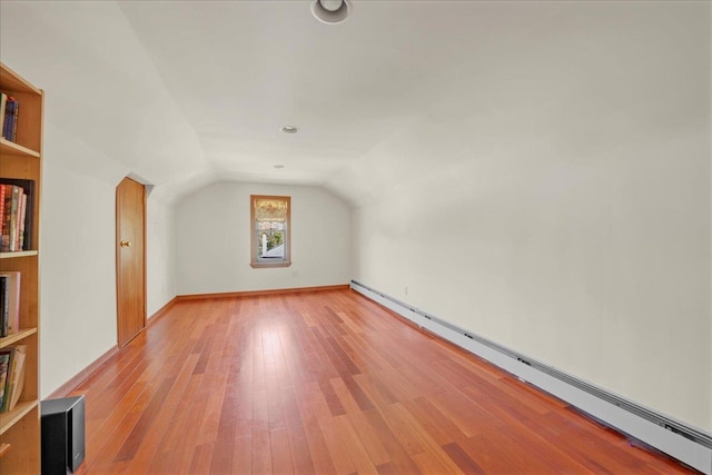 additional living space with a baseboard heating unit, vaulted ceiling, and light wood-style floors