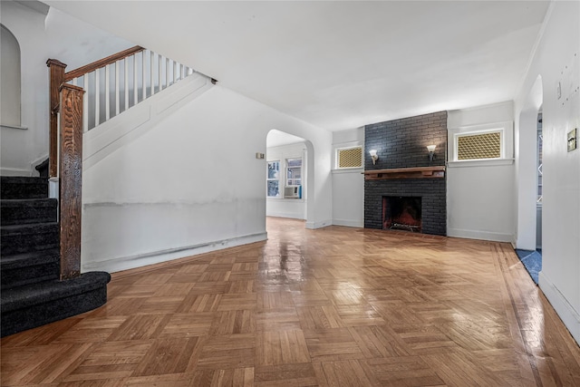 unfurnished living room featuring arched walkways, a brick fireplace, cooling unit, baseboards, and stairs