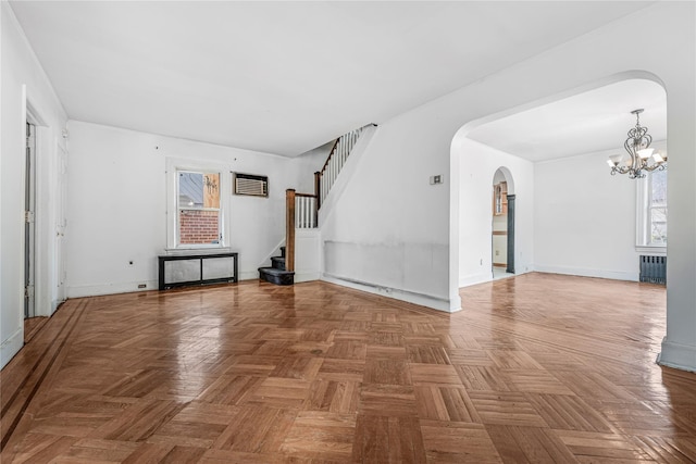 empty room featuring arched walkways, radiator, stairway, and baseboards