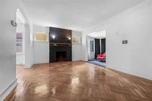 unfurnished living room with a brick fireplace, baseboards, and arched walkways