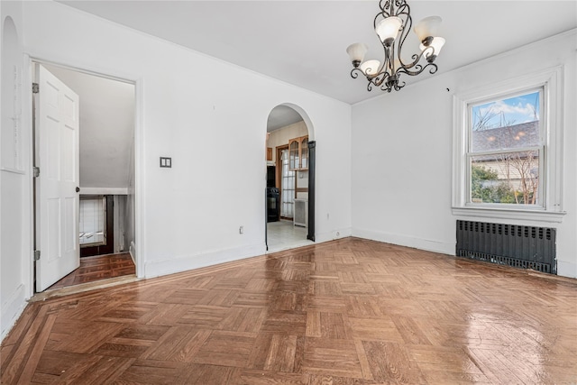 empty room featuring arched walkways, baseboards, a notable chandelier, and radiator