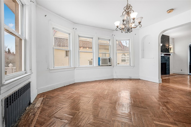 unfurnished dining area featuring baseboards, a fireplace, a notable chandelier, and radiator heating unit