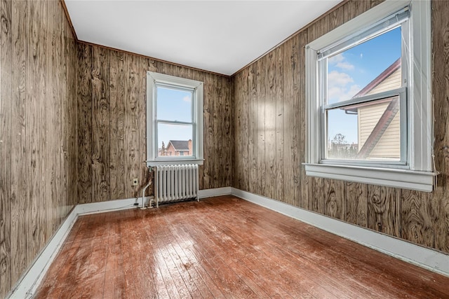 empty room featuring radiator, wood-type flooring, wooden walls, and baseboards