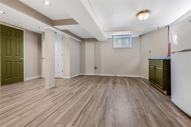 below grade area featuring light wood finished floors, recessed lighting, baseboards, and freestanding refrigerator