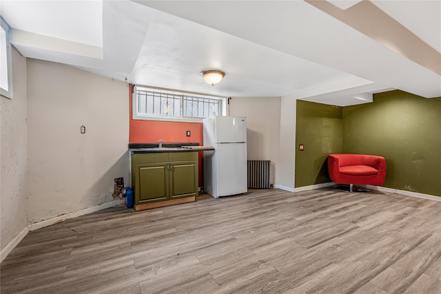 kitchen featuring radiator, light wood-style floors, green cabinetry, and freestanding refrigerator