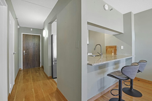 bar featuring a textured ceiling, light wood-style flooring, freestanding refrigerator, and a sink