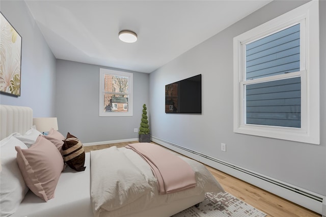 bedroom with a baseboard heating unit, baseboards, and wood finished floors