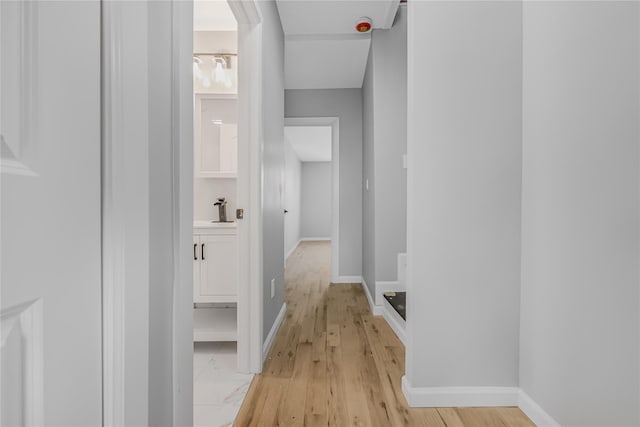 hall featuring light wood-type flooring, baseboards, and a sink