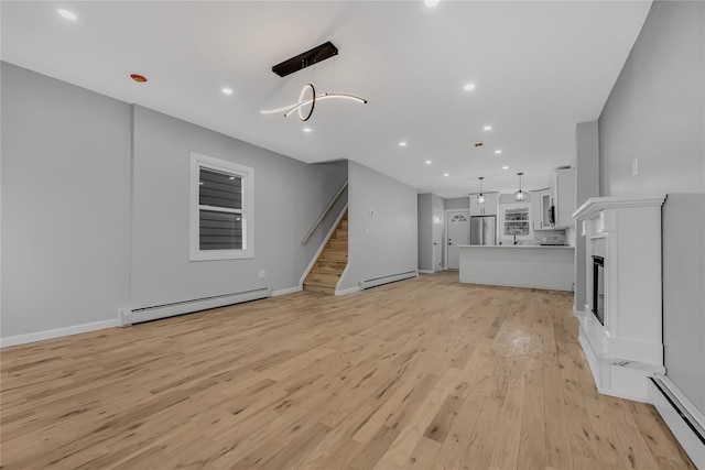 unfurnished living room featuring a baseboard heating unit, light wood-style floors, and stairs