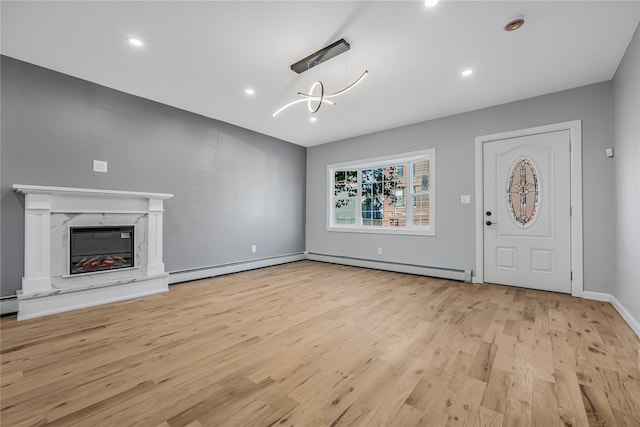 unfurnished living room with a baseboard radiator, a notable chandelier, wood finished floors, a high end fireplace, and baseboards