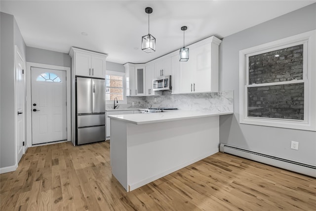 kitchen with appliances with stainless steel finishes, a peninsula, light countertops, white cabinetry, and backsplash