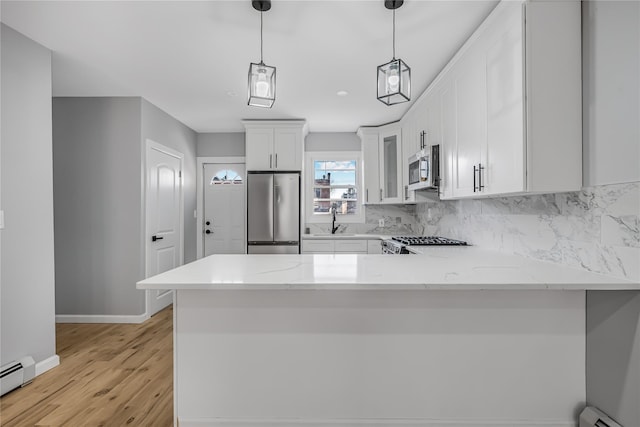 kitchen with a baseboard heating unit, a sink, white cabinets, appliances with stainless steel finishes, and tasteful backsplash