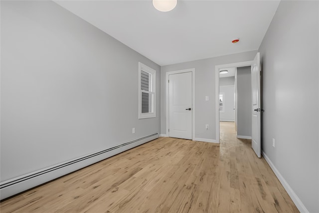 unfurnished bedroom with a baseboard radiator, baseboards, and light wood-style flooring