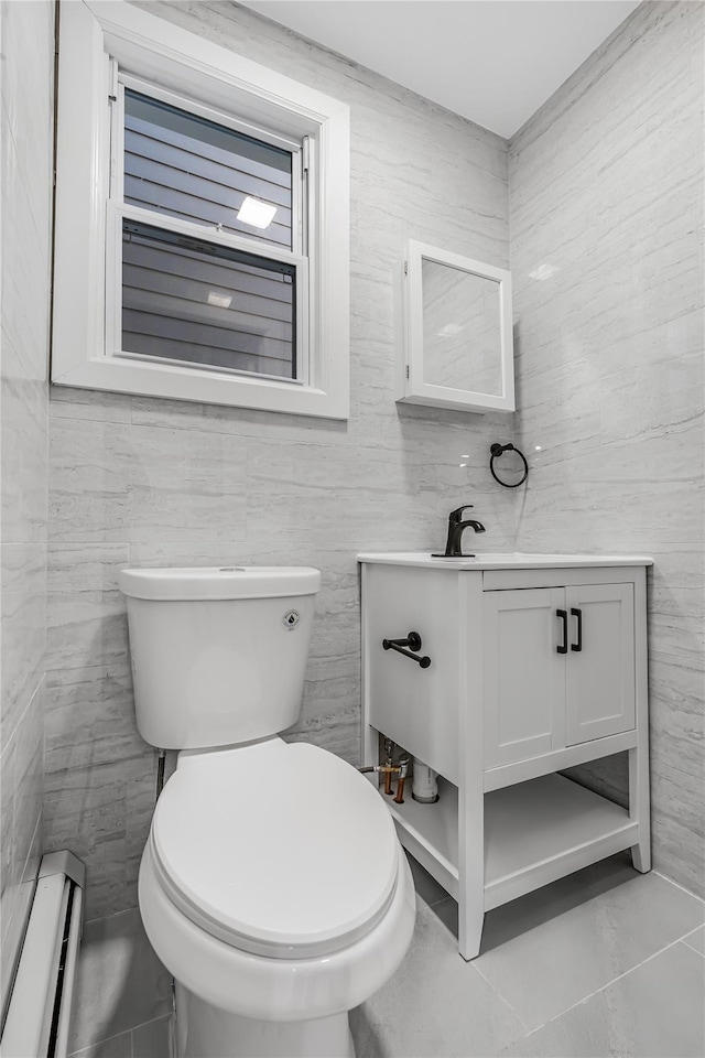 half bath with toilet, a baseboard radiator, tile walls, and vanity