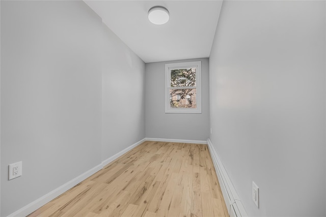 spare room with a baseboard heating unit, light wood-type flooring, and baseboards