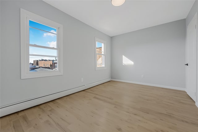 spare room featuring baseboard heating, light wood-type flooring, and baseboards