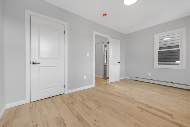 unfurnished bedroom with a baseboard radiator, baseboards, and light wood finished floors