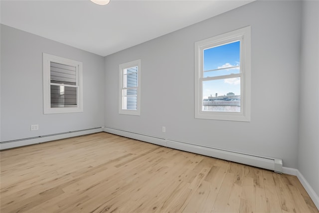 empty room featuring a baseboard heating unit, baseboards, and wood finished floors