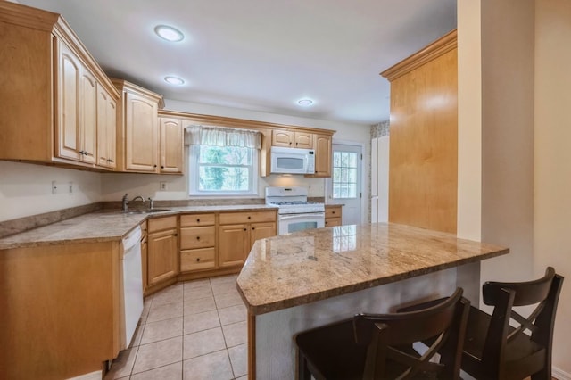 kitchen featuring white appliances, light tile patterned floors, a breakfast bar area, light brown cabinetry, and a sink