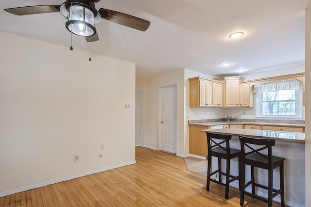 kitchen featuring baseboards, light countertops, light wood finished floors, and a kitchen breakfast bar