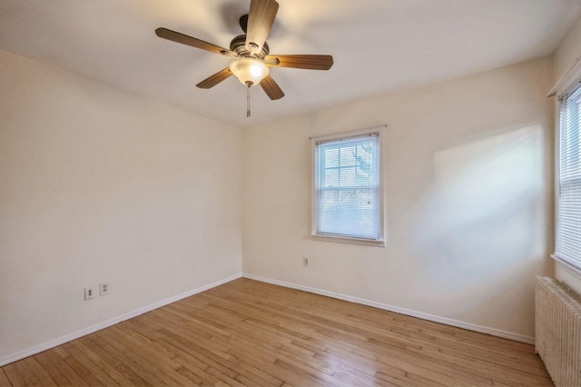 unfurnished room featuring baseboards, radiator heating unit, a ceiling fan, and light wood-style floors